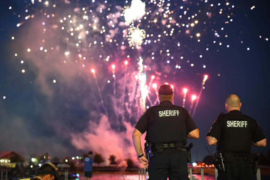 two sheriffs stand facing towards fireworks over a lake